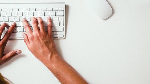 Zwei Hände liegen auf einer weißen Tastatur auf einem weißen Schreibtisch.